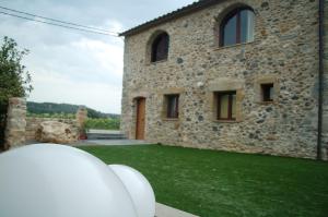 una casa de piedra con un césped verde delante de ella en Mas Font en Sant Gregori