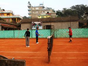 Tre persone sono in piedi su un campo da tennis di Pokhara Abroad Inn a Pokhara
