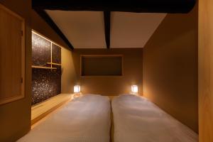 2 Betten in einem Zimmer mit Wandbeleuchtung in der Unterkunft Tsumugi Sanjusangendo in Kyoto