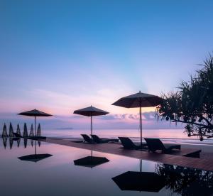 a pool with chairs and umbrellas and the ocean at Saai Resort in Bang Saphan Noi