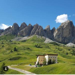 a house on a green hill with mountains in the background at Hotel Cir in Selva di Val Gardena