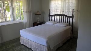 1 dormitorio con 1 cama con sábanas blancas y ventanas en Fairy Hill Palms, en Port Antonio