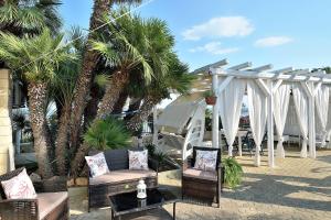 a patio with palm trees and chairs and a white pergola at Casa Mare Holiday Pozzallo in Pozzallo