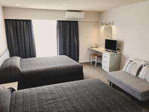ein Hotelzimmer mit 2 Betten und einem Schreibtisch in der Unterkunft The Village Inn Hotel in Te Anau