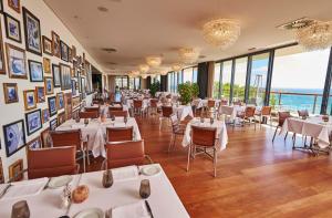 a restaurant with white tables and chairs and windows at Martinhal Sagres Beach Family Resort Hotel in Sagres