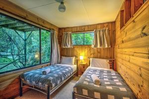 two beds in a room with wooden walls and windows at Beachcroft in Coles Bay