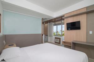 a bedroom with a large white bed and a tv at Xênius Hotel in João Pessoa