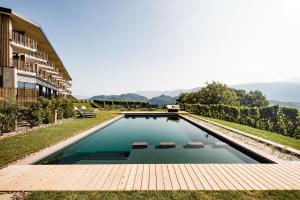 - une piscine avec une terrasse en bois à côté d'un bâtiment dans l'établissement Hotel Plattenhof, à Termeno