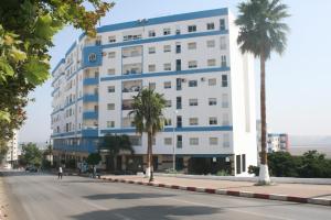 un grand bâtiment blanc avec des palmiers en face d'une rue dans l'établissement Appartement de Mustapha larache, à Larache