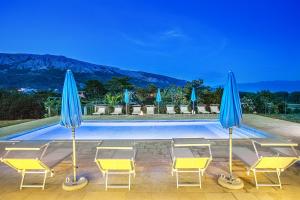 a pool with yellow chairs and blue umbrellas at Apartments Juranic I in Baška