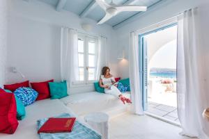 a woman sitting on a couch in a room with a window at Naxian Riviera Exclusive Seafront Suites, Junior Suite in Agios Prokopios