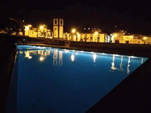 a blue swimming pool at night with buildings in the background at Casa da Ribeira in Povoação