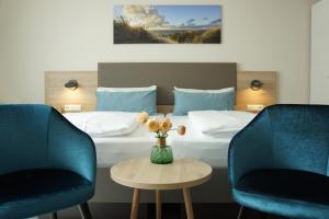 um quarto de hotel com uma cama e duas cadeiras e um vaso com flores em Hotel am Südwäldchen em Westerland