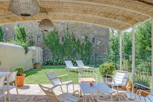un patio con sillas y mesas blancas y una pared de piedra. en La maison du Boulodrome, en La Bruguière