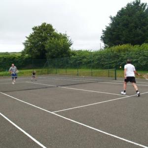 three people playing tennis on a tennis court at Coach House Cottage in Merton