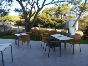 a patio with tables and chairs and a tree at Apartamentos Villa Primera in Cala Figuera