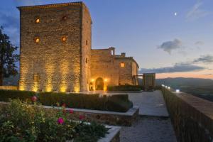 un grande edificio in pietra con una torre al tramonto di Castello di Velona Resort, Thermal SPA & Winery a Montalcino