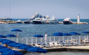 a man standing on a dock with blue umbrellas and boats at Hôtel Belles Rives in Juan-les-Pins