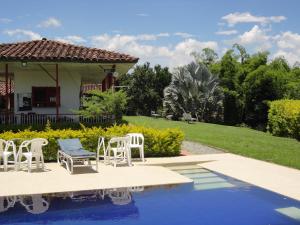 a pool with white chairs and a house at Finca Hotel Santana Campestre in Quimbaya