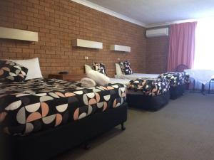 una camera d'albergo con tre letti e un muro di mattoni di James Street Motor Inn a Toowoomba