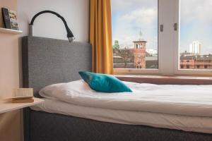 a bed with a blue pillow in a room with a window at Moment Hotels in Malmö