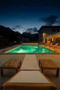 a swimming pool at night with two benches and a table at Hotel Posta in Forni di Sopra