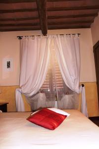 a bed with a red pillow in front of a window at Locanda La Mandragola in San Gimignano