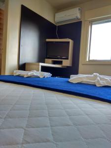 a room with a bed with a tv and a blue wall at Soratur Hotel & Coworking in Criciúma