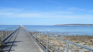 a boardwalk leading into the water with a lighthouse in the background at Wintersun Holiday Cottages in Emu Bay