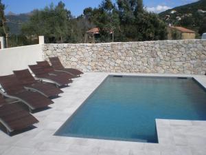 a swimming pool with chairs and a stone wall at Hôtel l'Alivu in Galeria