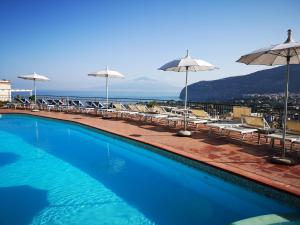 a swimming pool with chairs and umbrellas and the ocean at Hotel Cristina in Sorrento
