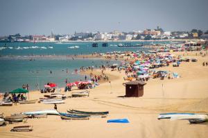 una multitud de personas en una playa con sombrillas en Playa de la Calzada, en Sanlúcar de Barrameda