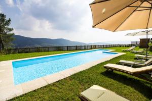 a swimming pool with an umbrella and some chairs and a table at Quinta da Baldieira in Mondim de Basto
