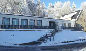 un edificio con nieve delante en Pension und Berggasthaus Kapellenstein, en Geyer