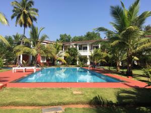 a swimming pool in front of a house with palm trees at Riverside Villa at Siolim in Siolim