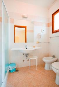 een badkamer met een wastafel, een toilet en een spiegel bij Hotel Marietta in Caorle