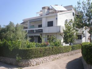una casa blanca con una pared de piedra y arbustos en Apartments Lukacic, en Krk