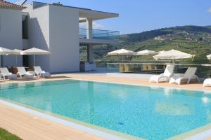 a swimming pool with chairs and umbrellas on a house at Delfim Douro Hotel in Lamego