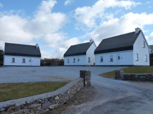 two white buildings with black roofs and a stone wall at Skellig Cottages in Ballinskelligs