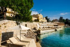 eine Gruppe Stühle und ein Regenschirm neben dem Wasser in der Unterkunft Villa Amalia - Liburnia in Opatija