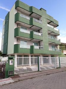 un bâtiment vert avec une clôture blanche devant lui dans l'établissement Residencial Júnior, à Bombinhas