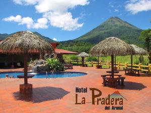 een resort met een zwembad met tafels en rieten parasols bij Hotel La Pradera del Arenal in Fortuna