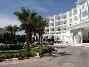 a large white building with palm trees in front of it at Chiraz Club - Families Only in Monastir