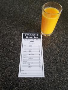 a glass of orange juice sitting next to a piece of paper at ASURE Phoenix Motor Inn in Blenheim