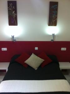 a bed with a red blanket and pillows on it at Hostal Neptuno in Cáceres
