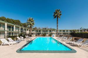una piscina con sillas y palmeras en un complejo en Days Inn by Wyndham Richmond Hill/Savannah, en Richmond Hill