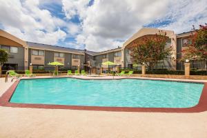 a pool with chairs and umbrellas in front of a building at Days Inn & Suites by Wyndham Corpus Christi Central in Corpus Christi