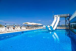 a pool with a water slide in front of a beach at Hotel New Castle in Cesenatico