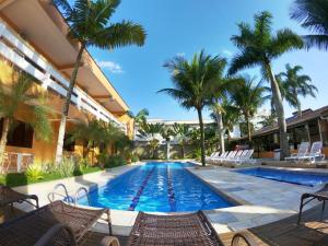 a swimming pool with chairs and palm trees at Pousada Acquaville PISCINA CLIMATIZADA in Bertioga