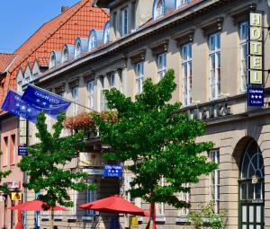 a building with flags and a tree in front of it at CityHotel Uelzen in Uelzen